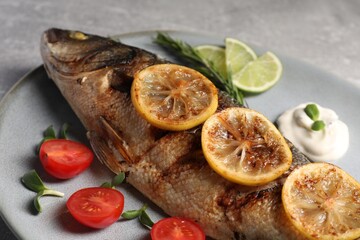 Delicious baked sea bass fish served with lemon, tomatoes and sauce on table, closeup