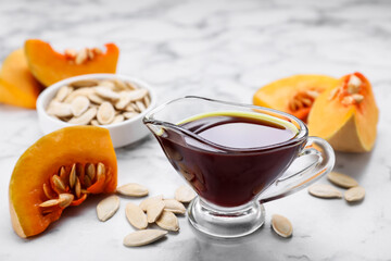 Fresh pumpkin seed oil in glass sauceboat on white marble table