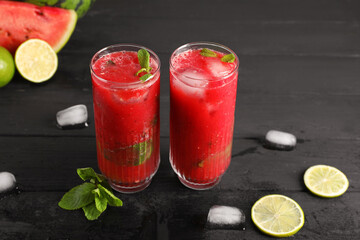 Glasses of delicious fresh watermelon juice, lime, mint and ice on black wooden table