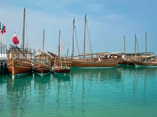 Traditional boats called dhows on the water in the bay in the daytime in Doha, Qatar on the coast of the Persian Gulf with the modern city skyline in the background.