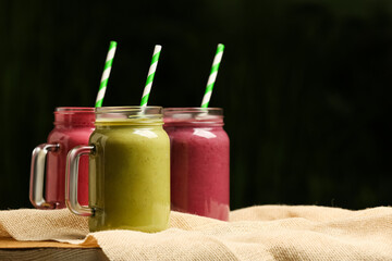 Different delicious smoothies in mason jars on table against dark background, space for text