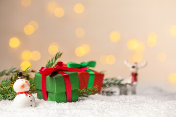 Gift boxes and Christmas decor on artificial snow against blurred festive lights, space for text