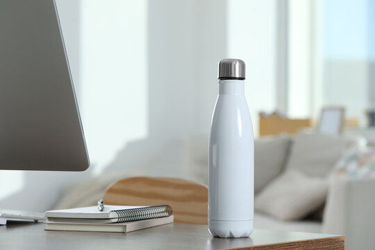 Stylish thermo bottle on wooden table at workplace in office