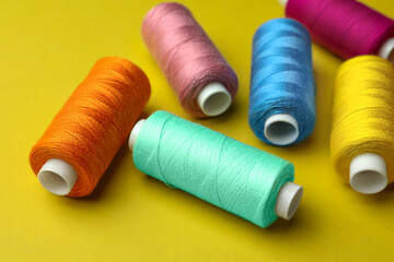 Different colorful sewing threads on yellow background