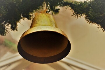 Weihnachtsdekoration mit goldener hängender Glocke aus Messing an grünem Tannenzweige vor weißem...