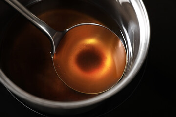 Saucepan and ladle with used cooking oil on stove, closeup