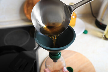 Woman pouring used cooking oil into bottle through funnel in kitchen, closeup