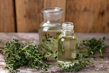Bottles of thyme essential oil and fresh plant on wooden table