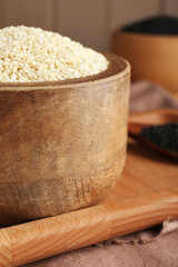 Bowl with white sesame seeds on wooden tray, closeup