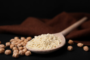 Spoon with chickpea flour and seeds on black table, closeup. Space for text