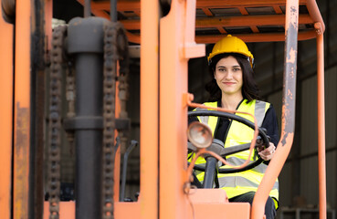 Female foreman wears hard hat driving forklift at shipping container yard, portrait. Young industrial engineer woman drives reach stacker truck to lift cargo box at logistic terminal dock.