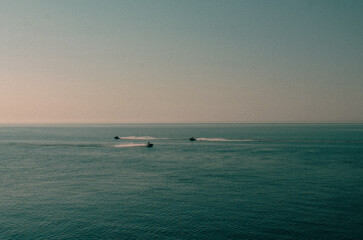 The sea surface, the horizon line separates the blue sea and the blue sky. Small silhouettes of vacationers riding jet skis.