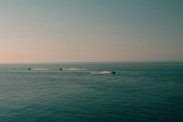 The sea surface, the horizon line separates the blue sea and the blue sky. Small silhouettes of vacationers riding jet skis.