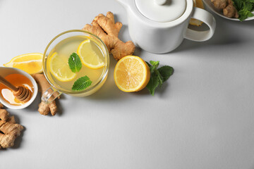 Delicious ginger tea and ingredients on light grey background, flat lay. Space for text