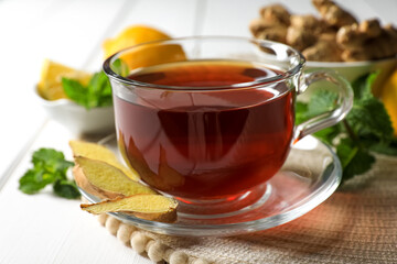Cup of delicious ginger tea and ingredients on white wooden table, closeup