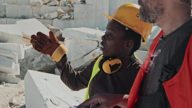 Ethnically diverse mine geologist and engineer holding sheet of paper with plan discussing marble extraction works