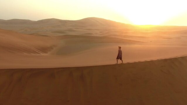 Man, walking and drone in desert or mountains of sand with sunset background. Person, travel and adventure for freedom or nature and gold land, carbon footprint in sand dunes of Namibia in Africa