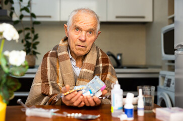 gray haired elderly man with handful of different medications in hand at home