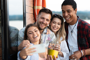 Group of multiracial friends on river boat enjoying in summer party, drinking cocktails and taking selfies