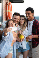 Group of multiracial friends on river boat enjoying in summer party, drinking cocktails and taking selfies