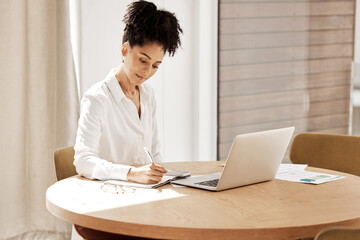 Woman writing in notebook, laptop on table and home office of accountant, auditor or financial advisor. Finance report, strategy and budget planning, black woman doing research on tax audit documents