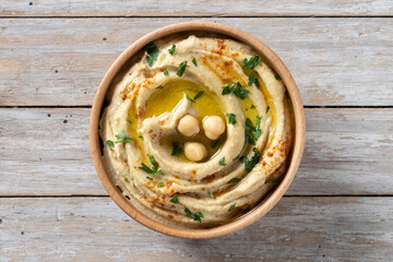Chickpea hummus in a wooden bowl garnished with parsley, paprika and olive oil on wooden table. Top...