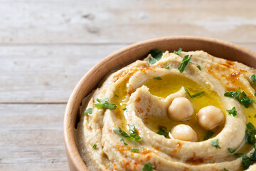 Chickpea hummus in a wooden bowl garnished with parsley, paprika and olive oil on wooden table....