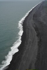Ocean with white foamy waves splashing into the black beach
