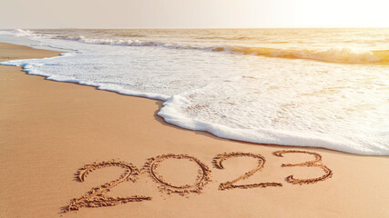 The year 2023- handwriting on sand beach, Happy New Year coming concept. White waves are lapping...
