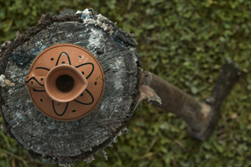 Traditional clay pitcher jug on a log in the yard of house with a rustic wooden fence background Old ceramic pot
