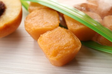 Frozen nectarine puree cubes in plastic bag on white wooden table, closeup