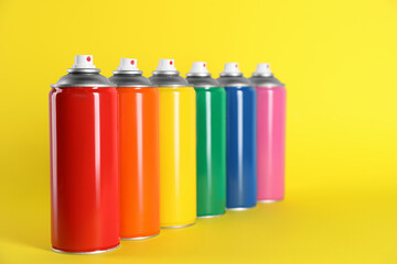 Colorful cans of spray paints on yellow background