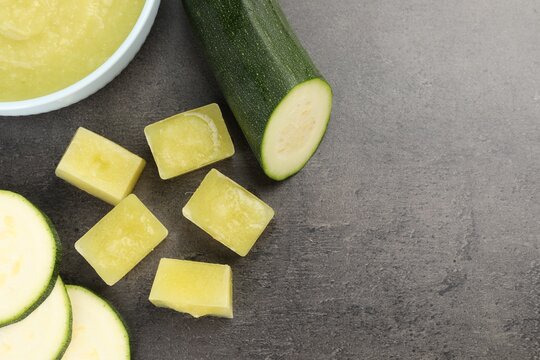 Frozen zucchini puree cubes and fresh zucchini on grey table, flat lay. Space for text