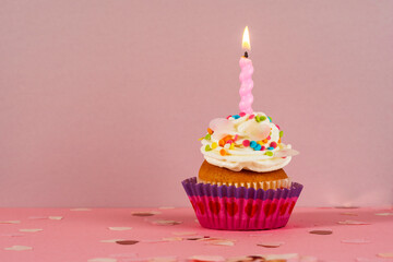 Birthday cupcake with candle light on a pink background. Cake with whyte cream and confectionery decor. Festive dessert and congratulations. Happy Birthday.