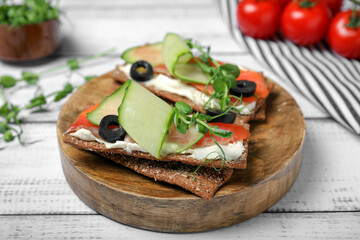 Tasty rye crispbreads with salmon, cream cheese and vegetables on white wooden table, closeup