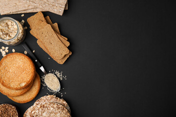 Rye crispbreads, rice cakes and rusks on black background, flat lay. Space for text