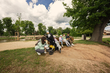 Mother with kids sitting and having rest in wooden bench outdoor in park.
