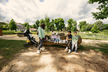 Obraz premium Mother with kids sitting and having rest in wooden bench outdoor in park.