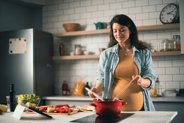 Beautiful pregnant woman preparing delicious food. Smiling woman preparing delicious food.
