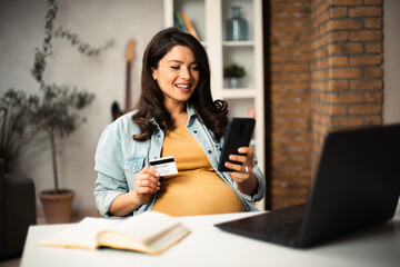 Pregnant woman shopping online at home. Happy woman with laptop and credit card.