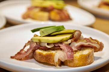Toast with bacon and avocado on a plate standing on a wooden table