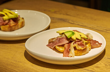 Toast with bacon and avocado on a plate standing on a wooden table
