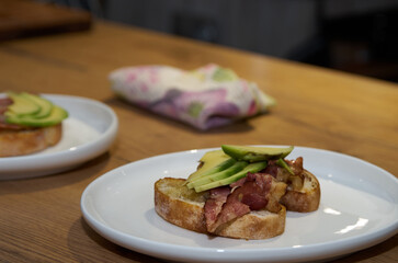 Toast with bacon and avocado on a plate standing on a wooden table