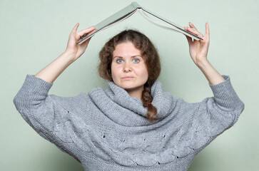 A woman hides under a book, as if under a roof from hostile factors: stress, depression, fear