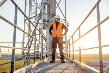 A proud height works worker is standing on top of the metal construction an looking at horizon.