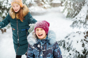 Fototapeta na wymiar Two happy girls are having fun and throws first snow on background of forest. Children play outdoors in snow. Outdoor fun for family Christmas vacation