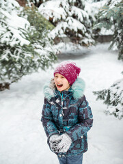 Fototapeta na wymiar Happy child girl are having fun and throwing snowball. Children play outdoors in snow. Outdoor fun for family in winter.