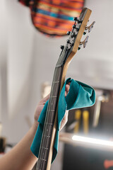 Hands of a man holding an electric bass guitar and cleaning its neck.