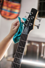 Hands of a man wiping the pins of an electric bass with a cloth in an instrument repair shop.