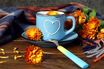 Cozy autumn tea party: a blue mug with a painted heart of chrysanthemums, a warm checkered scarf, a...